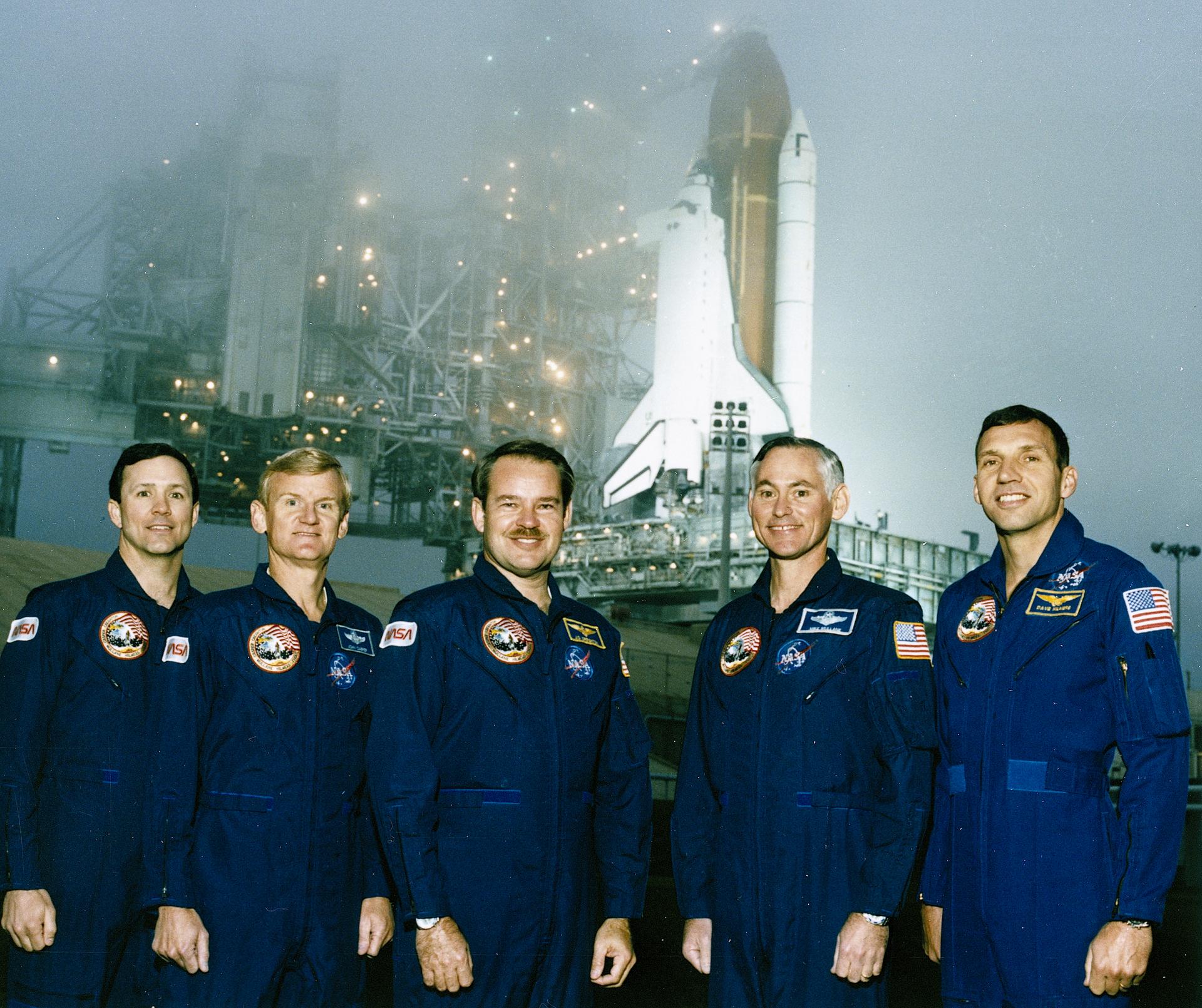 Five astronauts in blue jumpsuits Posed near the Space Shuttle Orbiter Discovery