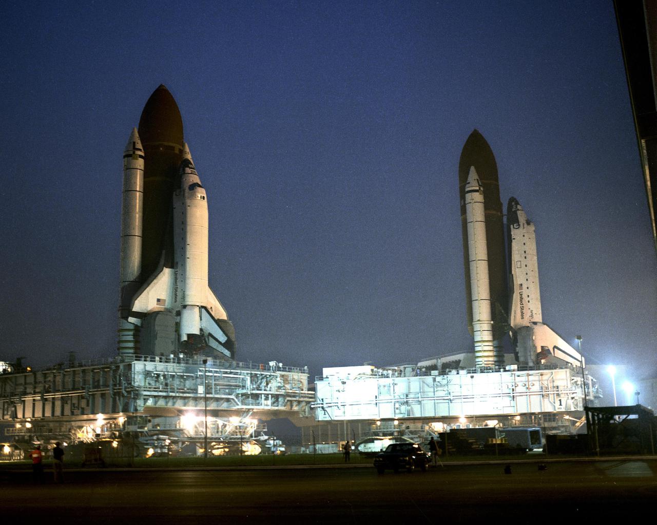 KENNEDY SPACE CENTER, FLA. --  The Space Shuttle Columbia (left), slated for mission STS-35, is rolled past the Space Shuttle Atlantis on its way to Pad 39A.  Atlantis, slated for mission STS-38, is parked in front of bay three of the Vehicle Assembly Building following its rollback from Pad 39A for repairs to the liquid hydrogen lines.  First motion of Atlantis from the pad was at 10:14 p.m. August 8.  It arrived at the VAB at 4 a.m. August 9.  First motion of Coumbia leaving the VAB for the pad was at 5:47 a.m.  Columbia is due to arrive at the pad at noon August 9.  Once Columbia is hard down at the pad, Atlantis will be moved into the VAB for destack operations.  When Columbia reaches the pad, its payload bay doors will be opened and servicing of the ASTRO-1 payload will begin.  Also, portions of the Shuttle interface verification test not completed in the VAB will be conducted.
