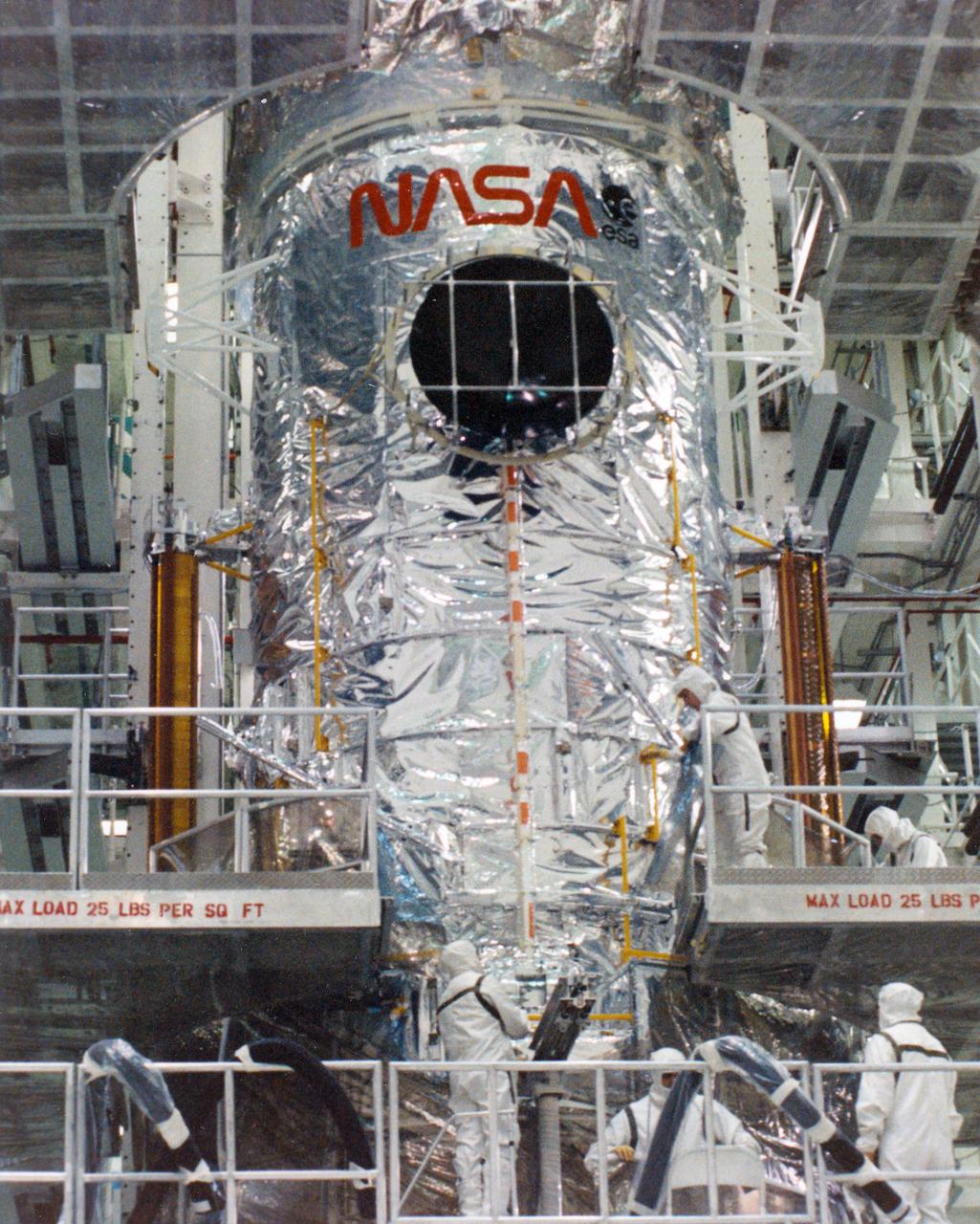 KENNEDY SPACE CENTER, FLA. -- In the Vertical Processing Facility at KSC, technicians begin to peel away the protective 'cocoon' from the lower portion of the Hubble Space Telescope (HST).  Removal from the upper portion has just been completed.  The cocoon is a sanitary liner which further assures cleanliness.  After the lower portion is cut away, there will be a final cleaning of the telescope and a contamination inspection.  A fresh cocoon will then be lowered over HST.  With HST, astronomers will be able to view 97 percent of the known universe, and will be able to get pictures unlimited and undistorted by the Earth's atmosphere. Compared with earth-based observatories, the HST will be able to view celestial objects that are 50 times fainter, provide images that are 10 times sharper, and see objects that are seven times farther away. .