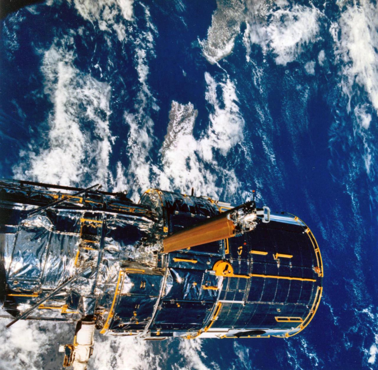 JOHNSON SPACE CENTER, HOUSTON, TEXAS-- STS-31 ONBOARD SCENE -- The Hubble Space Telescope (HST) is suspended in space by Discovery's remote manipulator system prior to deployment of its solar array panels and antennae and its ultimate release.  Puerto Rico and the Dominican Republic are recognizable at left of the frame.  The photo was taken with a handheld Hasselblad camera.  This was among the first photos NASA released on April 30 from the five-day mission.