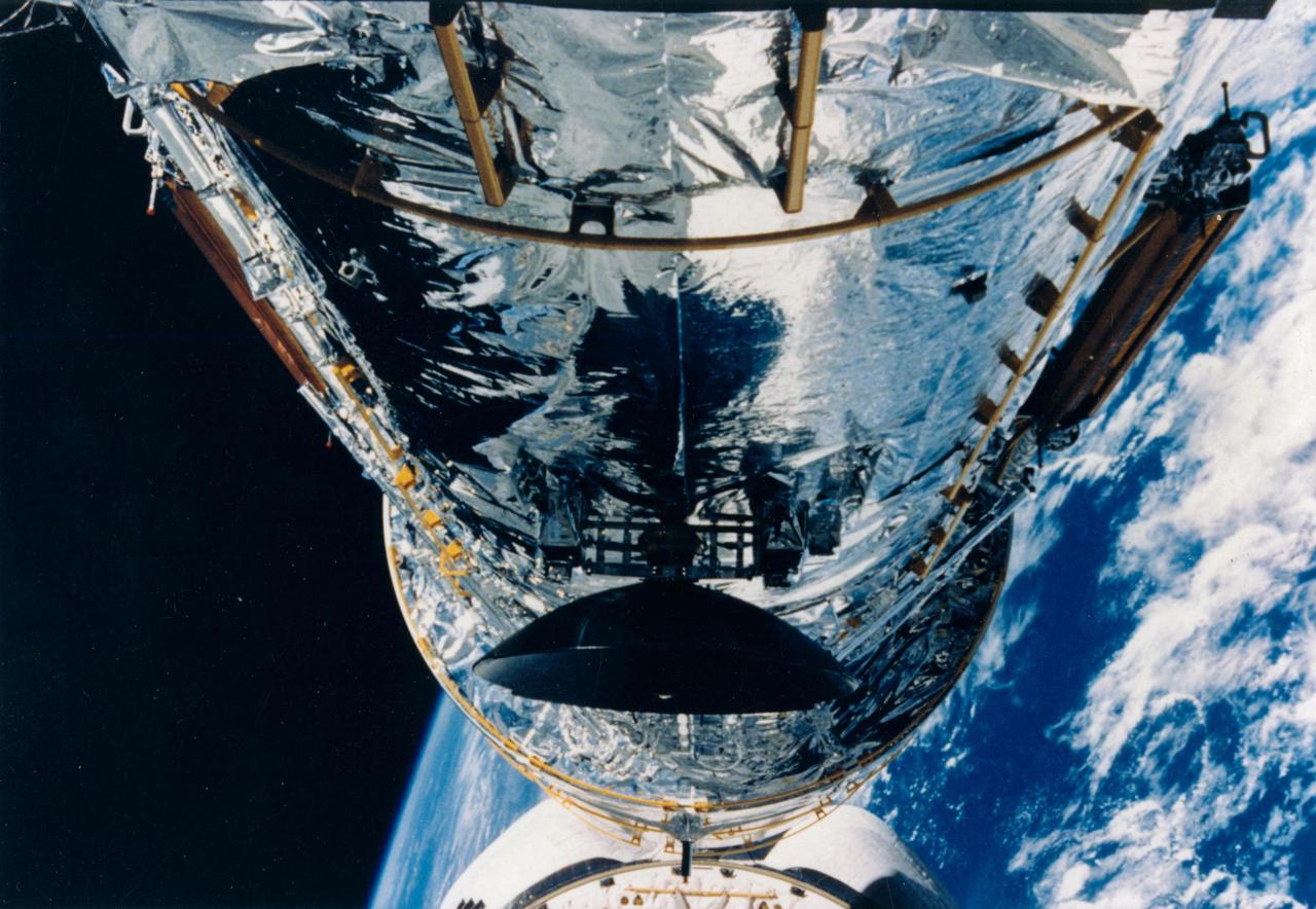 JOHNSON SPACE CENTER, HOUSTON, TEXAS-- STS-31 ONBOARD SCENE -- A medium closeup view photographed with fish-eye lens on a 35mm camera shooting the Hubble Space Telescope (HST) held above Discovery's cargo bay by the remote manipulator system prior to solar array and antennae deployment.