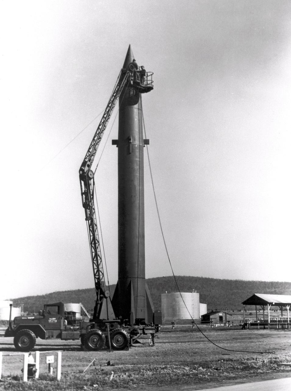 The image depicts Redstone missile being erected. The Redstone ballistic missile was a high-accuracy, liquid-propelled, surface-to-surface missile developed by Army Ballistic Missile Agency, Redstone Arsenal, in Huntsville, Alabama, under the direction of Dr. von Braun. The Redstone engine was a modified and improved version of the Air Force's Navaho cruise missile engine of the late forties. The A-series, as this would be known, utilized a cylindrical combustion chamber as compared with the bulky, spherical V-2 chamber. By 1951, the Army was moving rapidly toward the design of the Redstone missile, and the production was begun in 1952. Redstone rockets became the "reliable workhorse" for America's early space program. As an example of the versatility, Redstone was utilized in the booster for Explorer 1, the first American satellite, with no major changes to the engine or missile