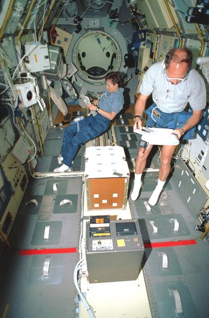 Onboard Space Shuttle Discovery (STS-42) Astronaut Norman E. Thagard, payload commander, and Canadian payload specialist Roberta L. Bondar are busily engaged with experiments in the International Microgravity Laboratory (IML-1) science module. Bondar reads a checklist near the Biorack while Thagard performs a VCR tape change-out. The two, along with four other NASA astronauts and a second IML-1 payload specialist spent more than eight days conducting experiments in Earth orbit. Part of the Space Acceleration Measurement System is in center foreground.