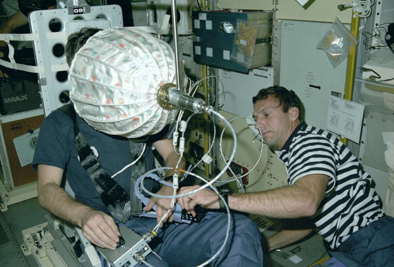 Astronaut Ulf Merbold on the stationary seat of the mini-sled, stares into an umbrella-shaped rotating dome with colored dots. Astronaut Merbold, assisted by astronaut David Hilmer, are conducting the Visual Simulator Experiment, a space physiology experiment. The Visual Stimulator Experiment measures the relative importance of visual and vestibular information in determining body orientation. When a person looks at a rotating visual field, a false sensation of self-rotation, called circularvection, results. In weightlessness, circularvection should increase immediately and may continue to increase as the nervous system comes to rely more on visual than vestibular cues. As Astronaut Merbold stares into the rotating dome with a pattern of colored dots and its interior, he turns a knob to indicate his perception of body rotation. The strength of circularvection is calculated by comparing signals from the dome and the knob. The greater the false sense of circularvection, the more the subject is relying on visual information instead of otolith information. The IML-1 mission was the first in a series of Shuttle flights dedicated to fundamental materials and life sciences research with the international partners. The participating space agencies included: NASA, the 14-nation European Space Agency (ESA), the Canadian Space Agency (CSA), the French National Center of Space Studies (CNES), the German Space Agency and the German Aerospace Research Establishment (DAR/DLR), and the National Space Development Agency of Japan (NASDA). Managed by the Marshall Space Flight Center, IML-1 was launched on January 22, 1992 aboard the Space Shuttle Orbiter Discovery (STS-42 mission).