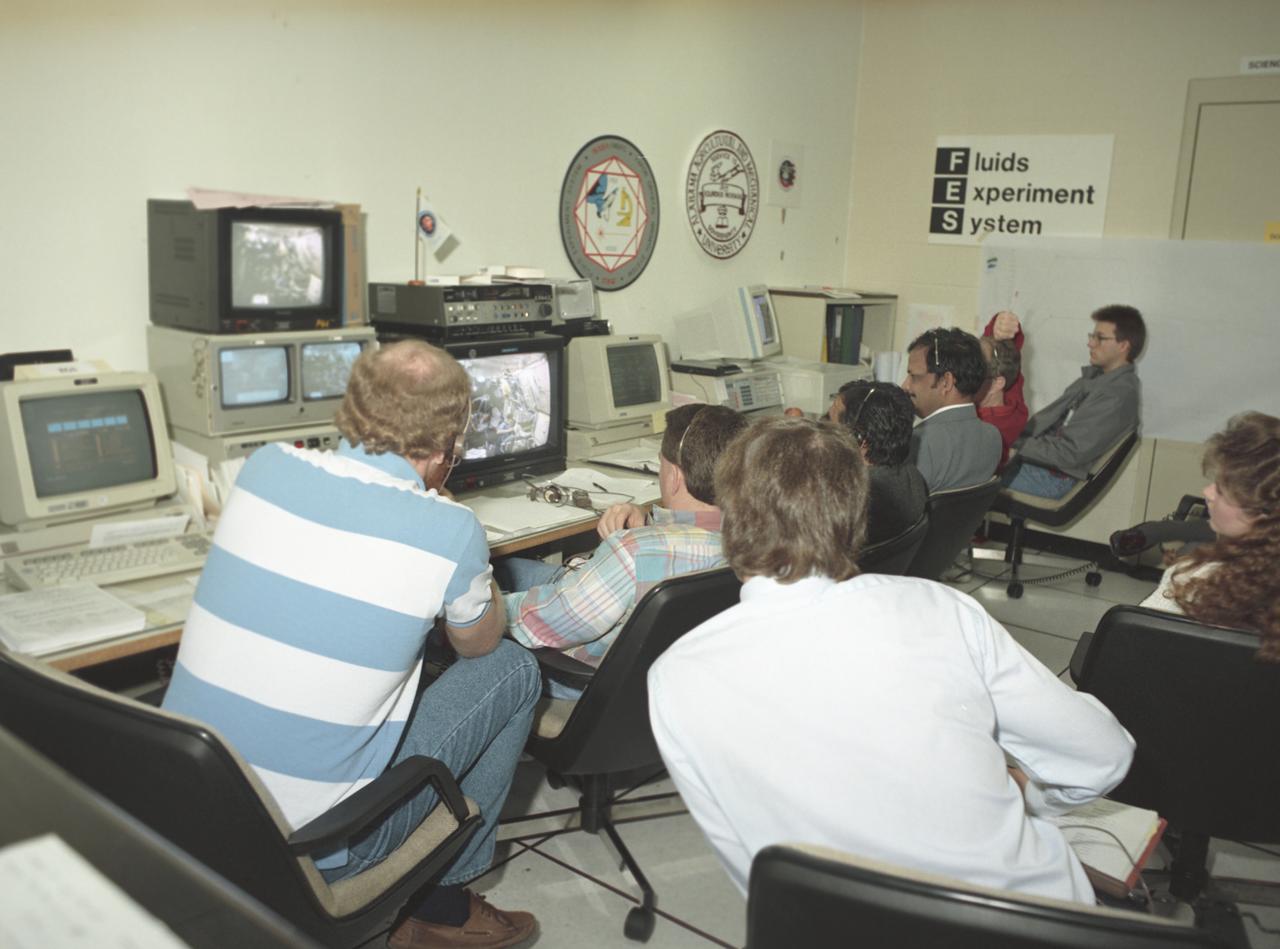 This photograph shows activities during the International Microgravity Laboratory-1 (IML-1) mission (STS-42) in the Payload Operations Control Center (POCC) at the Marshall Space Flight Center. Members of the Fluid Experiment System (FES) group monitor the progress of their experiment through video at the POCC. The IML-1 mission was the first in a series of Shuttle flights dedicated to fundamental materials and life sciences research. The mission was to explore, in depth, the complex effects of weightlessness on living organisms and materials processing. The crew conducted experiments on the human nervous system's adaptation to low gravity and the effects on other life forms such as shrimp eggs, lentil seedlings, fruit fly eggs, and bacteria. Low gravity materials processing experiments included crystal growth from a variety of substances such as enzymes, mercury, iodine, and virus. The International space science research organizations that participated in this mission were: The U.S. National Aeronautics and Space Administion, the European Space Agency, the Canadian Space Agency, the French National Center for Space Studies, the German Space Agency, and the National Space Development Agency of Japan. The POCC was the air/ground communication charnel used between astronauts aboard the Spacelab and scientists, researchers, and ground control teams during the Spacelab missions. The facility made instantaneous video and audio communications possible for scientists on the ground to follow the progress and to send direct commands of their research almost as if they were in space with the crew.