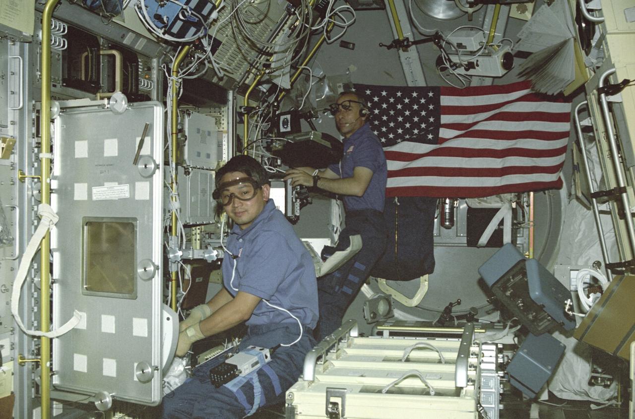 In this photograph, astronaut Eugene Trinh, a payload specialist for this mission, is working at the Drop Physics Module (DPM), and mission specialist Carl Meade is working on the experiment at the Glovebox inside the first United States Microgravity Laboratory (USML-1) Science Module. The USML-1 was one of NASA's missions dedicated to scientific investigations in a microgravity environment inside the Spacelab module. Investigations aboard the USML-1 included: materials science, fluid dynamics, biotechnology (crystal growth), and combustion science. The DPM is dedicated to the detailed study of the dynamics of fluid drops in microgravity. The Glovebox offers experimenters new capabilities and technologies in microgravity with a clean working space and minimizes contamination risks to both Spacelab and experiment samples. Payload specialists are professional scientists or engineers whose only assignment on a space flight is to carry out scientific and technological experiments. Their specific training for a space flight is usually limited to a short period of learning how to live and work in weightlessness. Mission Specialists are both professional scientists and career astronauts. Thus they are a link or bridge between the other crew members, and combine the functions of resident maintenance engineers, in-space counterparts of flight engineers in aircraft, and fully qualified scientists. The USML-1 flew aboard the STS-50 mission on June 1992, and was managed by the Marshall Space Flight Center.