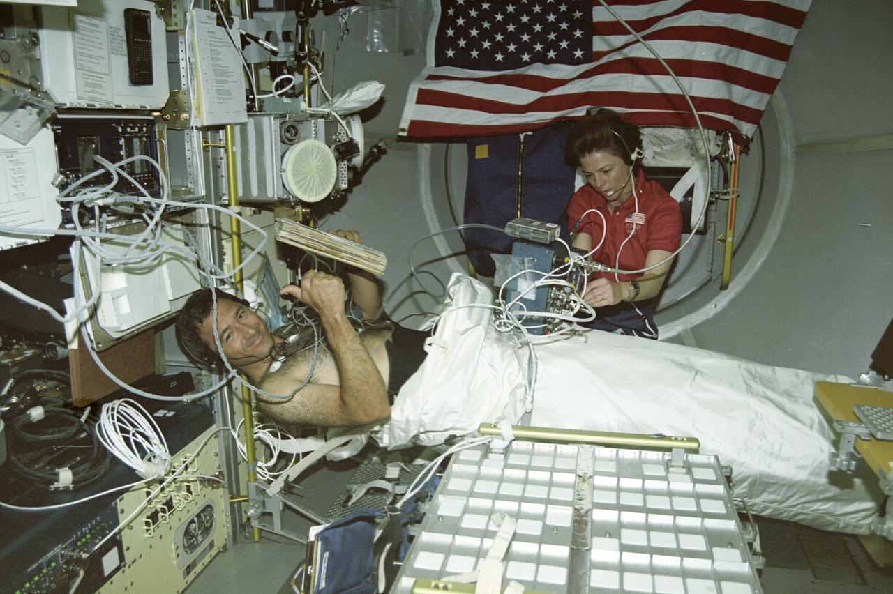 The first United States Microgravity Laboratory (USML-1) flew in orbit inside the Spacelab science module for extended periods, providing scientists and researchers greater opportunities for research in materials science, fluid dynamics, biotechnology (crystal growth), and combustion science. In this photograph, Astronaut Bornie Dunbar and Astronaut Larry DeLucas are conducting the Lower Body Negative Pressure (LBNP) experiment, which is to protect the health and safety of the crew and to shorten the time required to readapt to gravity when they return to Earth. When humans go into space, the lack of gravity causes many changes in the body. One change is that fluids normally kept in the lower body by gravity, shift upward to the head and chest. This is why astronauts' faces appear chubby or puffy. The change in fluid volume also affects the heart. The reduced fluid volume means that there is less blood to circulate through the body. Crewmembers may experience reduced blood flow to the brain when returning to Earth. This leads to fainting or near-fainting episodes. With the use of LBNP to simulate the pull of gravity in conjunction with fluids, salt tablets can recondition the cardiovascular system. This treatment, called "soak," is effective up to 24 hours. The LBNP uses a three-layer collapsible cylinder that seals around the crewmember's waist which simulates the effects of gravity and helps pull fluids into the lower body. The data collected will be analyzed to determine physiological changes in the crewmembers and effectiveness of the treatment. The USML-1 was launched aboard the Space Shuttle Orbiter Columbia (STS-50) on June 25, 1992.