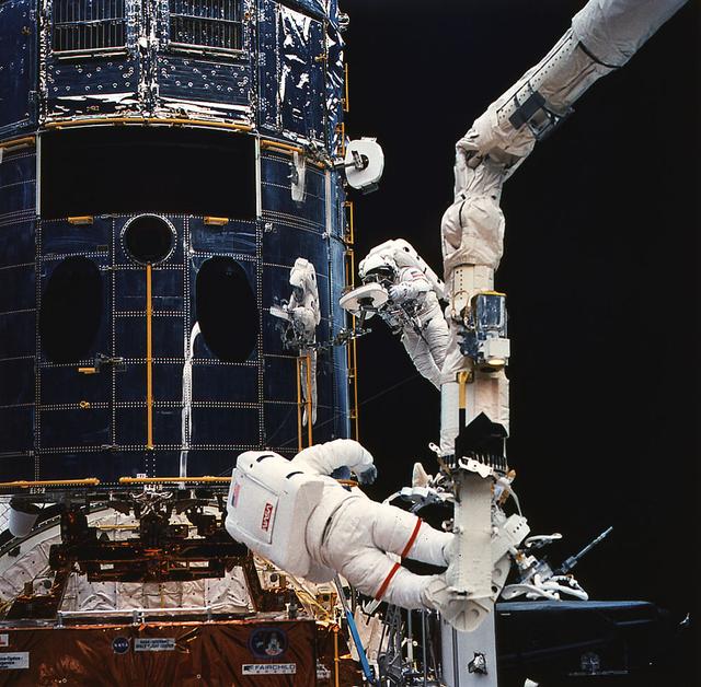 Anchored on the end of orbiter Endeavour's remote manipulator system arm, astronaut Jeffrey Hoffman (foreground) prepares to install the new wide field planetary camera into the empty cavity of the Hubble Space Telescope (HST). Astronaut Story Musgrave works with a portable foot restraint.