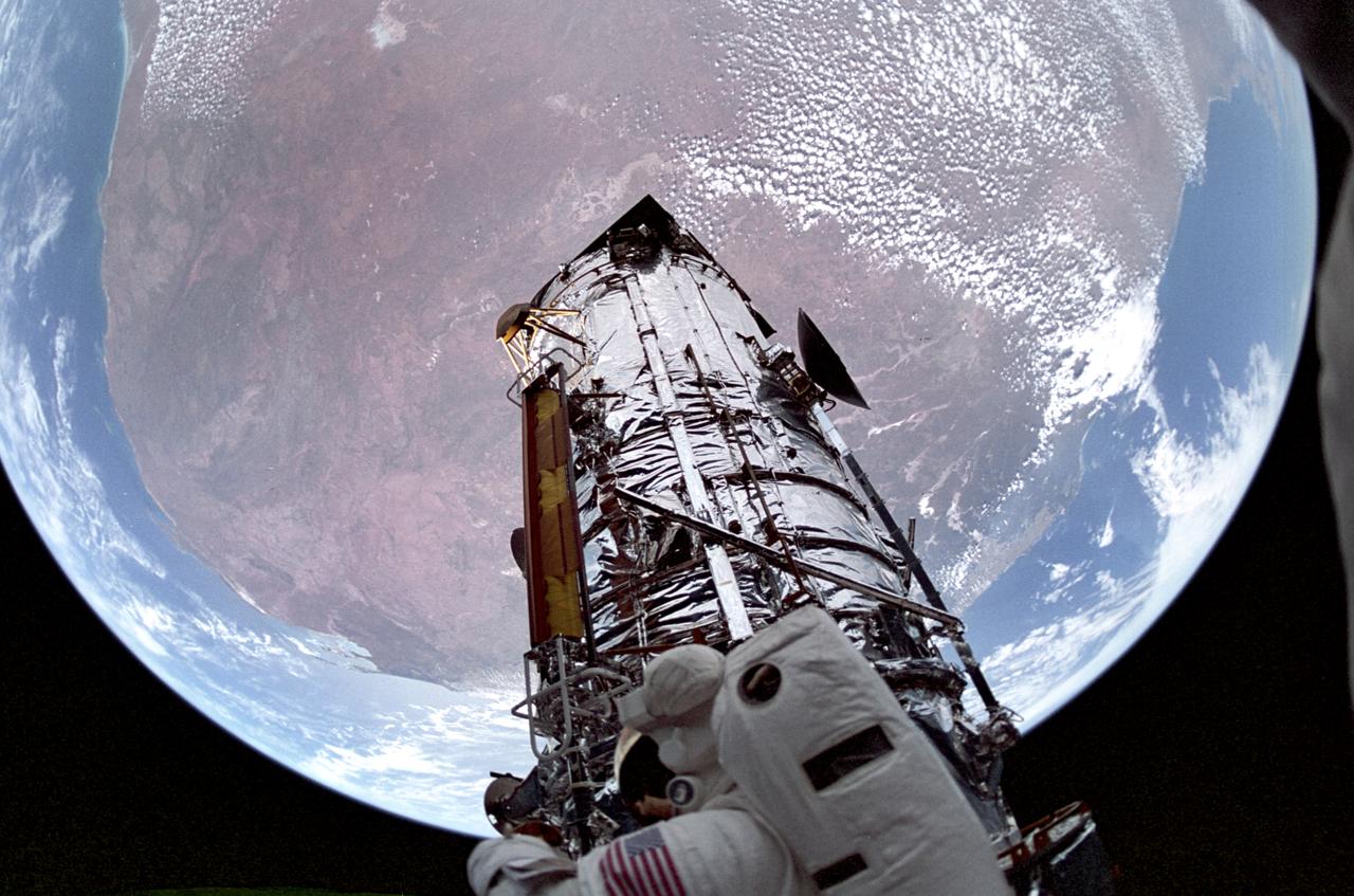 Backdropped against the Earth, the Hubble Space Telescope (HST)is shown sporting new and modified solar arrays stowed against its barrel. Orbiting Earth at an altitude of 325 nautical miles, an astronaut begins other repairs of the HST while perched atop a foot restraint on shuttle Endeavour's remote manipulator system arm. The 59th and final Shuttle flight of 1993 was one of most challenging and complex marned missions ever attempted. During record five back-to-back space walks totaling 35 hours and 28 minutes, two teams of astronauts completed the first servicing of the HST. The STS-061 mission was launched aboard Space Shuttle Endeavor on December 2, 1993.