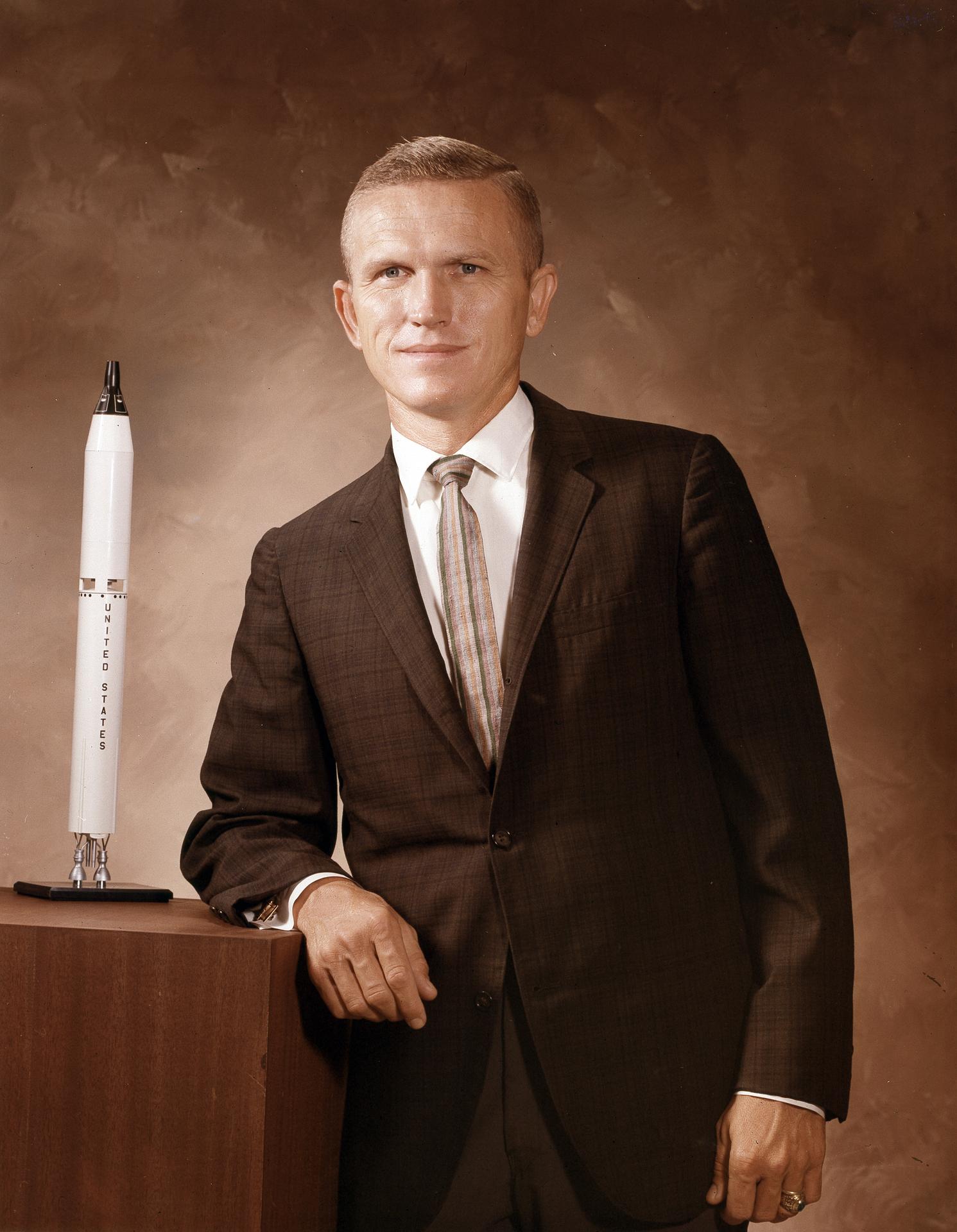 Portrait of Frank Borman leaning on a cabinet with a model of a rocket