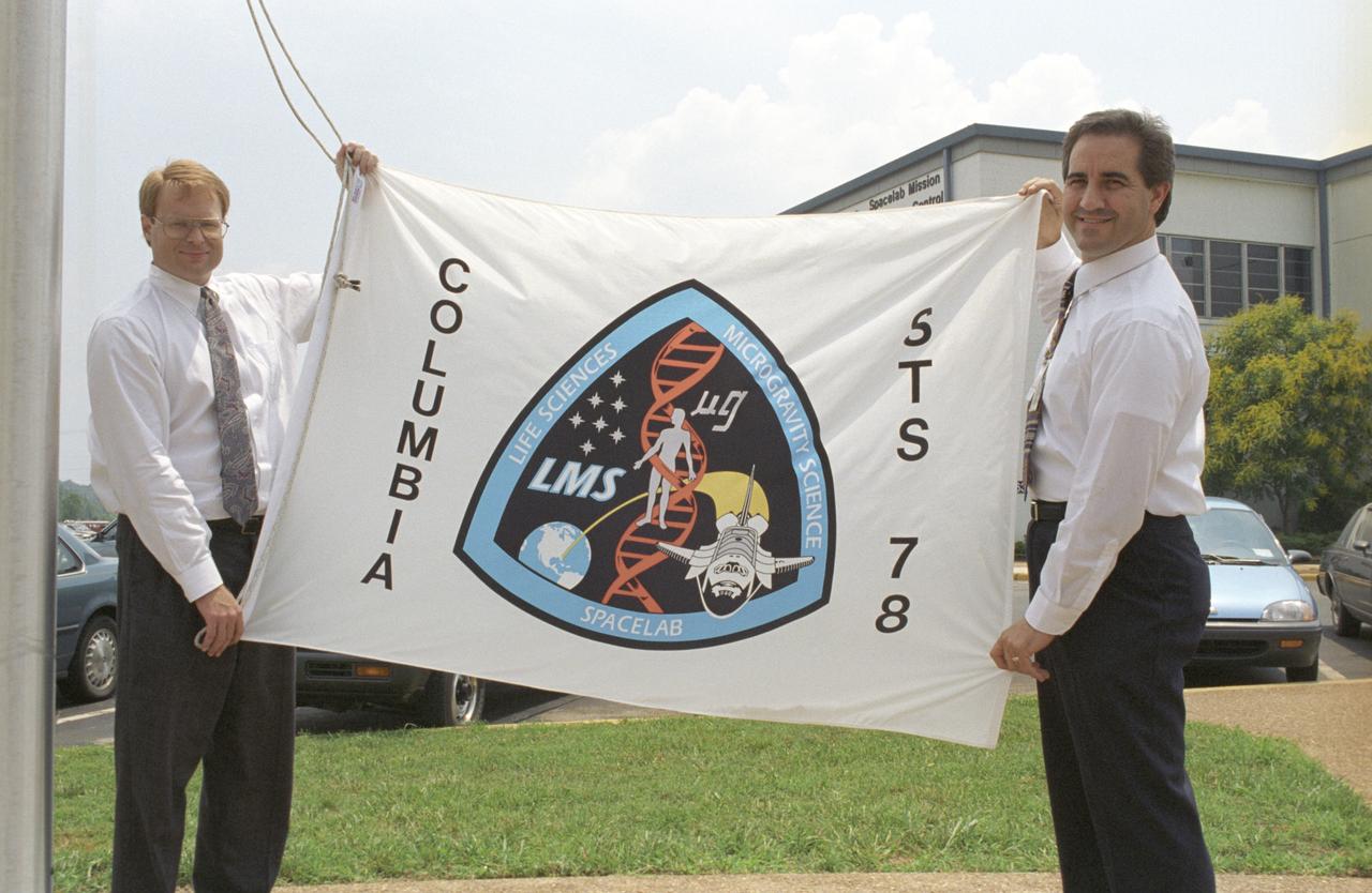 Launched on June 20, 1996, the STS-78 mission’s primary payload was the Life and Microgravity Spacelab (LMS), which was managed by the Marshall Space Flight Center (MSFC). During the 17 day space flight, the crew conducted a diverse slate of experiments divided into a mix of life science and microgravity investigations. In a manner very similar to future International Space Station operations, LMS researchers from the United States and their European counterparts shared resources such as crew time and equipment. Five space agencies (NASA/USA, European Space Agency/Europe (ESA), French Space Agency/France, Canadian Space Agency /Canada, and Italian Space Agency/Italy) along with research scientists from 10 countries worked together on the design, development and construction of the LMS. In this photo, LMS mission scientist Patton Downey and LMS mission manager Mark Boudreaux display the flag that was flown for the mission at MSFC.