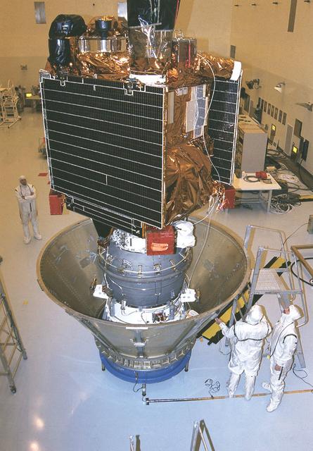 Workers at the Jet Propulsion Research Lab (JPL) in the Payload Hazardous Servicing Facility (PHSF) prepare the Mars Global Surveyor spacecraft for transfer to the launch pad by placing it in a protective canister. The Surveyor spacecraft (upper) is already mated to its solid propellant upper stage booster (lower), which is actually the third stage of the Delta II expendable launch vehicle that will propel the spacecraft on its interplanetary journey to Mars.