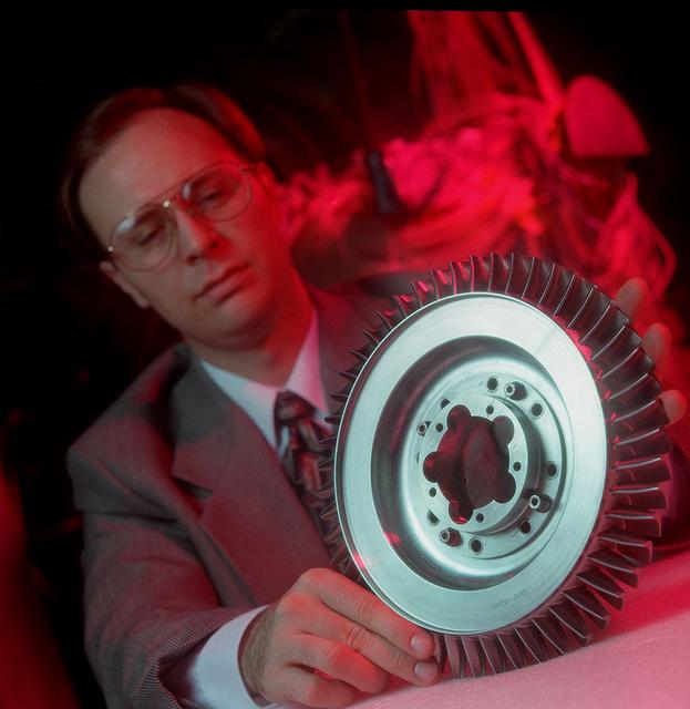 A NASA scientist displays Space Shuttle Main Engine (SSME) turbine component which underwent air flow tests at Marshall's Structures and Dynamics Lab. Such studies could improve efficiency of aircraft engines, and lower operational costs.