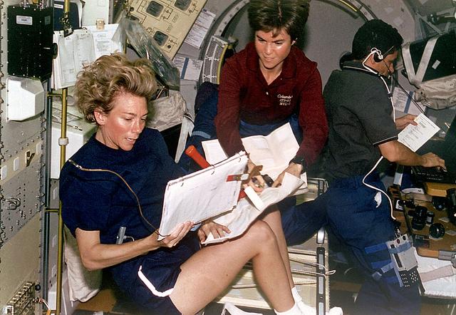 This Space Shuttle Columbia (STS-94) onboard photo is of astronauts Susan Still and Janice Voss reviewing an Inflight Maintenance (IFM) procedure in the Microgravity Science Lab (MSL-1) science module. Astronaut Gregory Linteris works at a lap top computer in the background.
