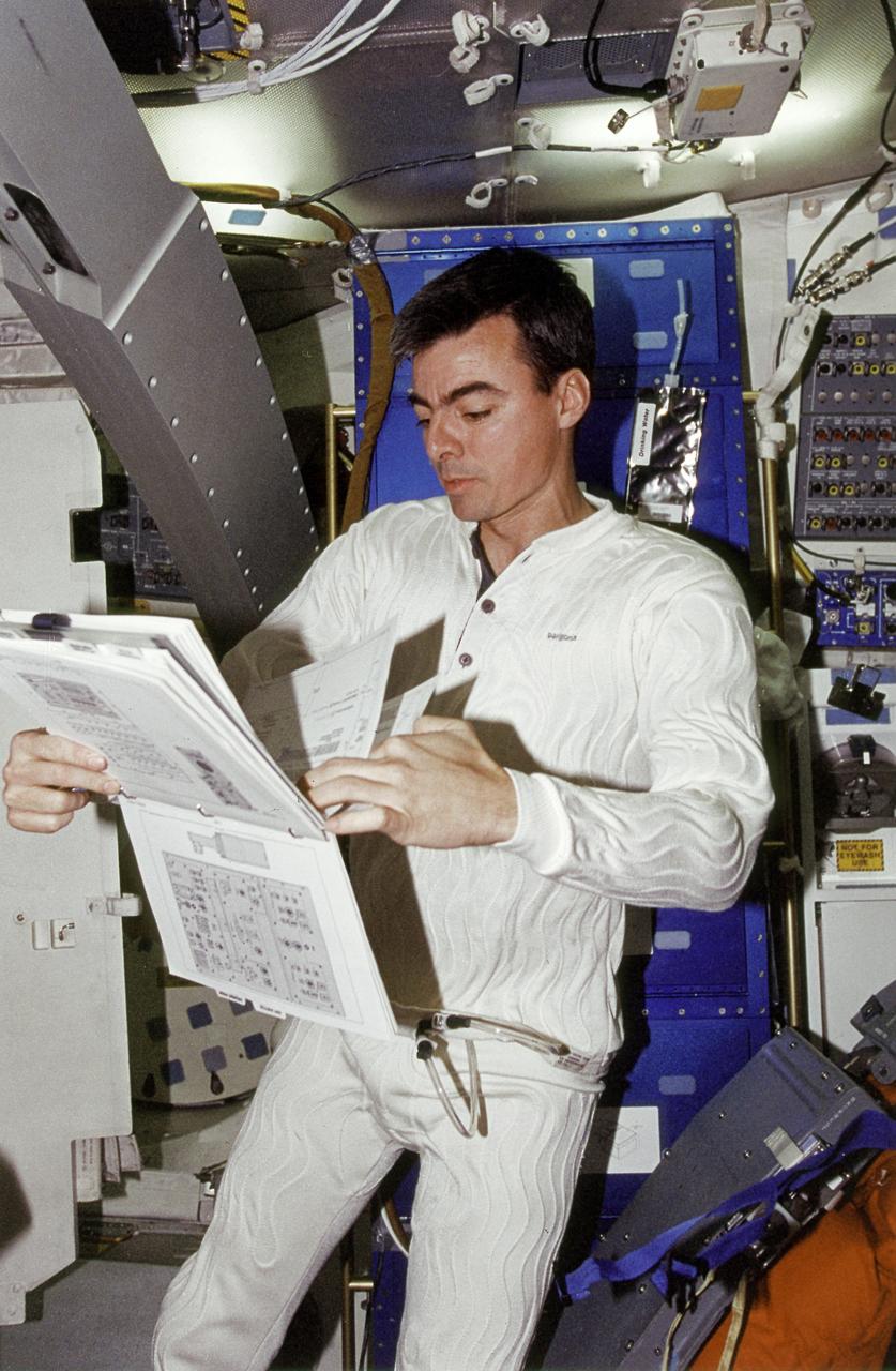 Onboard Space Shuttle Columbia (STS-62) Pilot Andrew M. Allen looks over a procedures book in the midst of a 14-day mission. Allen is attired in a new thermally controlled undergarment. Allen wore the garment during the launch and entry phases of the flight.