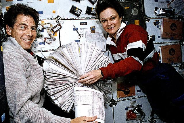 Astronaut Tamara Jernigan, STS-67 payload commander, and payload specialist Samuel T. Durrance use the absence of gravity for a perusal of Astro-2 targets in a loose-leaf, Rolodex-type collection of data. The two are in the mid-deck of the Earth-orbiting Space Shuttle Endeavour.