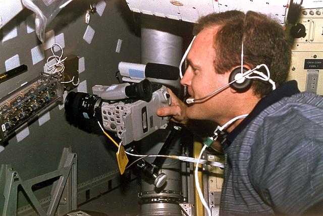 Astronaut James D. Halsell, Jr., mission commander, uses a Hi-8mm camcorder to videotape the Hand Held Diffusion Test Cells (HHDTC), in the Spacelab Science Module aboard the Earth-orbiting Space Shuttle Columbia (STS-94). Each test cell has three chambers containing a protein solution, a buffer solution and a precipitant solution chamber. Using the liquid-liquid diffusion method, the different fluids are brought into contact but not mixed. Over a period of time, the fluids will diffuse into each other through the random motion of molecules. The gradual increase in concentration of the precipitant within the protein solution causes the proteins to crystallize.
