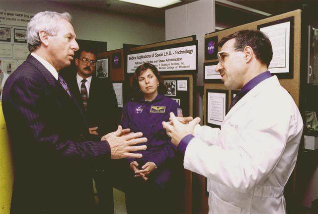 NASA Administrator Dan Goldin (left), during a visit at Children's Hospital of Wisconsin in Milwaukee, Wisconsin, discussed how NASA's special lighting technology may soon treat cancer. Goldin talked with Dr.Harry Whelan (right) and Dr. Kerneth Reichert (center left), both pediatric neurologists with the Hospital and professors at the Medical College of Wisconsin in Milwaukee. Accompanied by Astronaut Mary Ellen Weber, Goldin was shown this innovative treatment, called Photodynamic Therapy, a method used to destroy the tumor without damaging the delicate brain tissue around it. The treatment uses tiny pinhead-size Light Emitting Diodes (LEDs) developed for Space Product Development plant growth experiments.