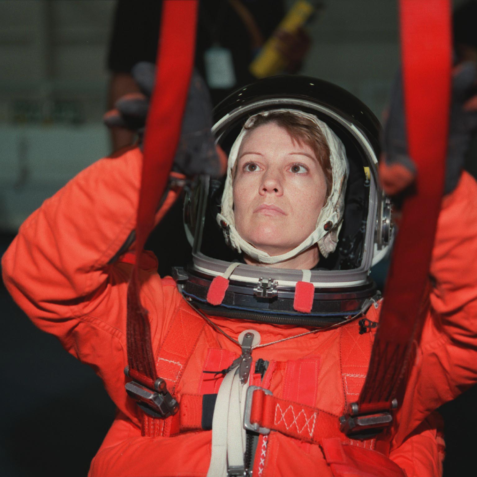 Woman in an orange spacesuit wearing a parachute for training.