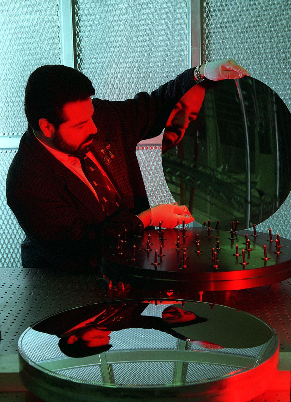 NASA's Space Optics Manufacturing Center has been working to expand our view of the universe via sophisticated new telescopes. The Optics Center's goal is to develop low-cost, advanced space optics technologies for the NASA program in the 21st century - including the long-term goal of imaging Earth-like planets in distant solar systems. To reduce the cost of mirror fabrication, Marshall Space Flight Center (MSFC) has developed replication techniques, the machinery, and materials to replicate electro-formed nickel mirrors. The process allows fabricating precisely shaped mandrels to be used and reused as masters for replicating high-quality mirrors. Dr. Joe Ritter examines a replicated electro-formed nickel-alloy mirror which exemplifies the improvements in mirror fabrication techniques, with benefits such as dramtic weight reduction that have been achieved at the Marshall Space Flight Center's Space Optics Manufacturing Technology Center (SOMTC).