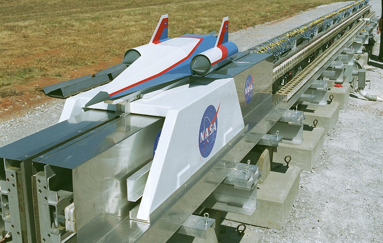 In this photograph, a futuristic spacecraft model sits atop a carrier on the Magnetic Launch Assist System, formerly known as the Magnetic Levitation (MagLev) System, experimental track at the Marshall Space Flight Center (MSFC). Engineers at MSFC have developed and tested Magnetic Launch Assist technologies that would use magnetic fields to levitate and accelerate a vehicle along a track at very high speeds. Similar to high-speed trains and roller coasters that use high-strength magnets to lift and propel a vehicle a couple of inches above a guideway, a Magnetic Launch Assist system would electromagnetically drive a space vehicle along the track. A full-scale, operational track would be about 1.5-miles long and capable of accelerating a vehicle to 600 mph in 9.5 seconds. This track is an advanced linear induction motor. Induction motors are common in fans, power drills, and sewing machines. Instead of spinning in a circular motion to turn a shaft or gears, a linear induction motor produces thrust in a straight line. Mounted on concrete pedestals, the track is 100-feet long, about 2-feet wide, and about 1.5-feet high. The major advantages of launch assist for NASA launch vehicles is that it reduces the weight of the take-off, the landing gear, the wing size, and less propellant resulting in significant cost savings. The US Navy and the British MOD (Ministry of Defense) are planning to use magnetic launch assist for their next generation aircraft carriers as the aircraft launch system.  The US Army is considering using this technology for launching target drones for anti-aircraft training. 