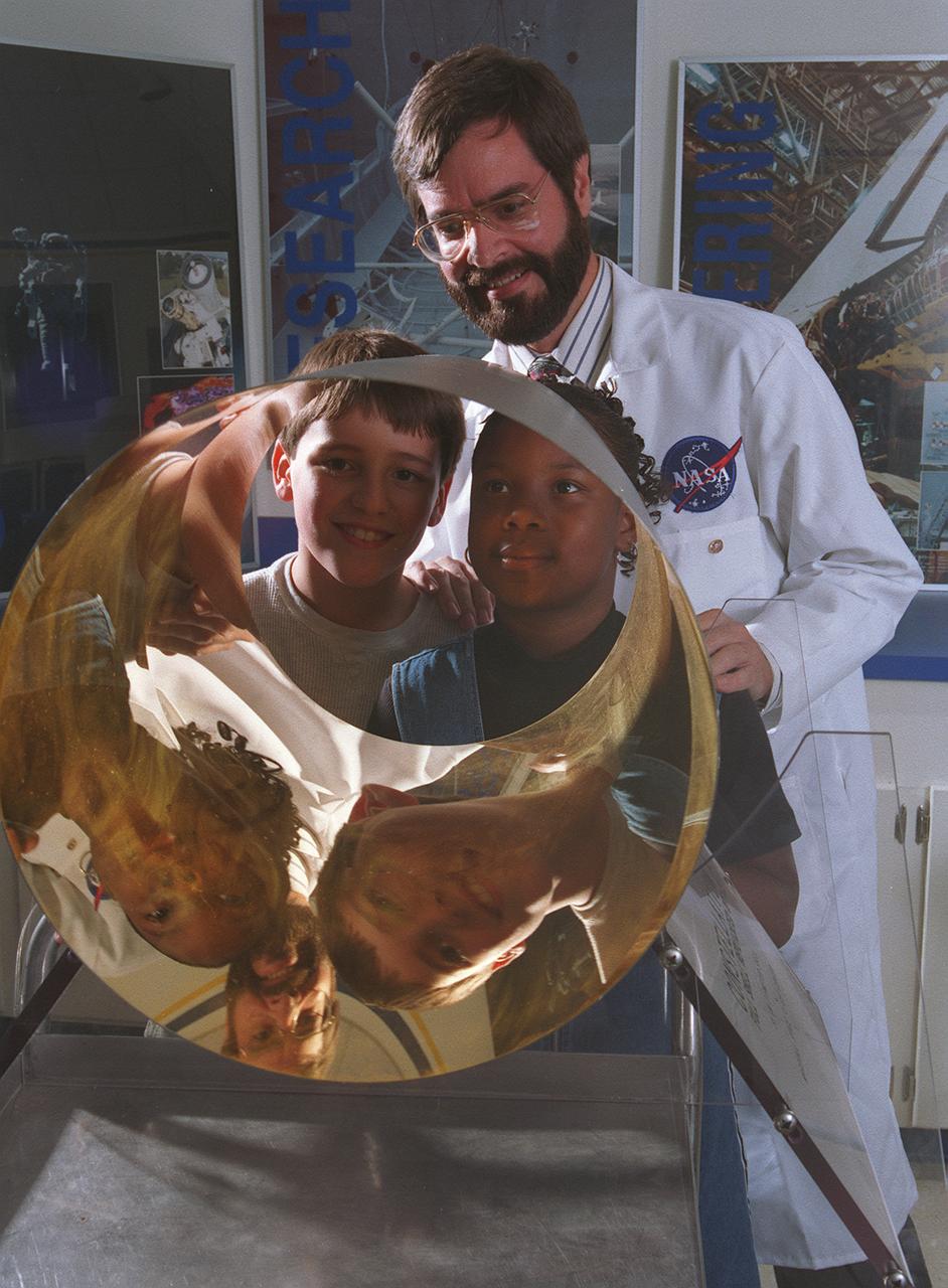 Through Marshall Space Flight Center (MSFC) Education Department, over 400 MSFC employees have volunteered to support educational program during regular work hours. Project LASER (Learning About Science, Engineering, and Research) provides support for mentor/tutor requests, education tours, classroom presentations, and curriculum development. This program is available to teachers and students living within commuting distance of the NASA/MSFC in Huntsville, Alabama (approximately 50-miles radius). This image depicts students viewing their reflections in an x-ray mirror with Marshall optic engineer Vince Huegele at the Discovery Laboratory, which is an onsite MSFC laboratory facility that provides hands-on educational workshop sessions for teachers and students learning activities. 