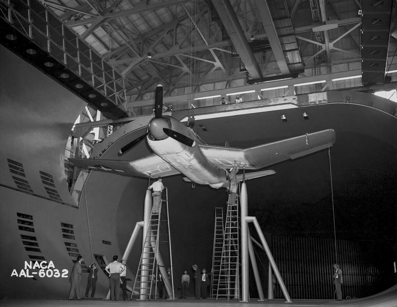 Test section of the Ames 40 x 80 foot wind tunnel with the overhead doors open.  XSB2D-1 airplane being lowered onto the struts by the overhead crane. Mechanics and engineers on orchard ladders aligning the model with ball sockets on the struts. The Douglas BTD Destroyer was an American dive/ torpedo bomber developed for the United States Navy during World War II.