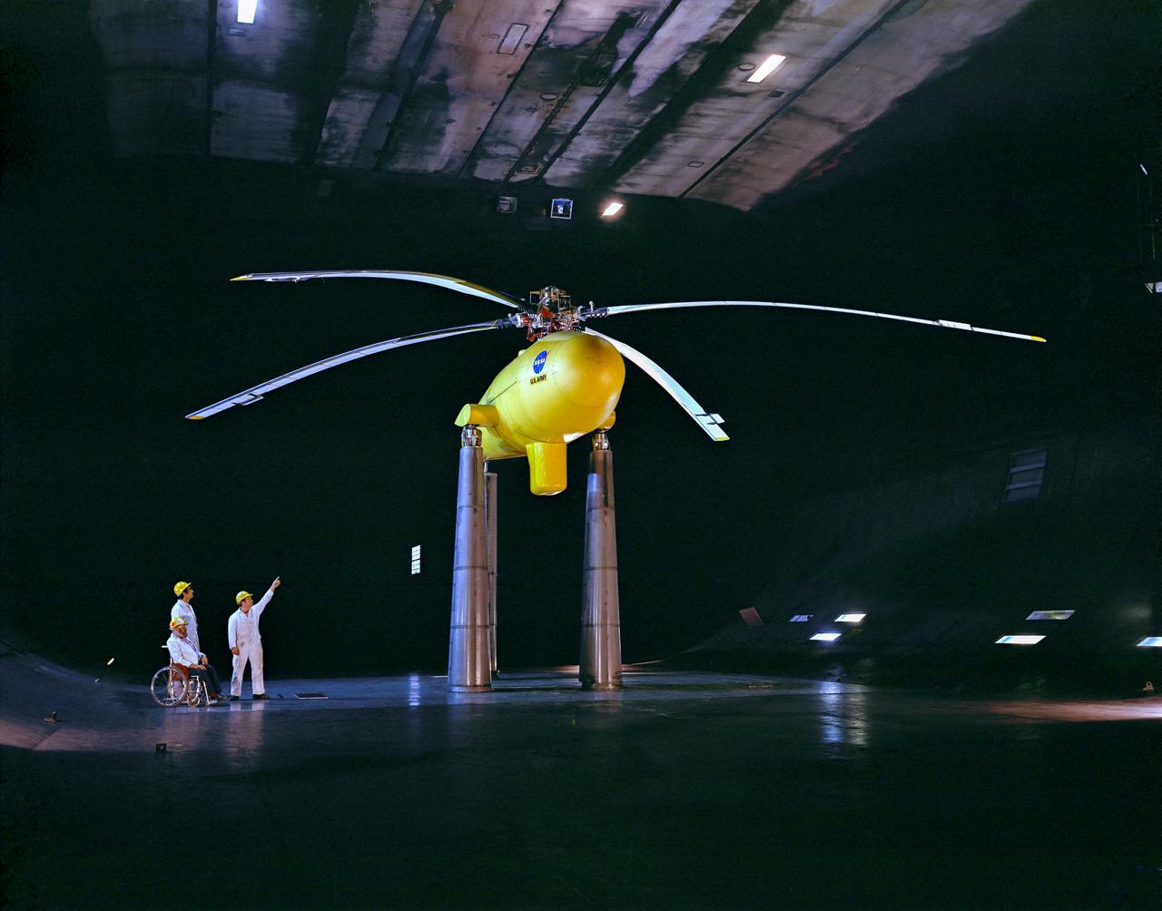 3/4 lower front view of Controllable Twist Rotor (CTR) test of 4 blade helicopter model.  Pictures with Ben Mandwyler Andy Lemnios, John McCloud (wheel chair), in 40x80 foot wind tunnel.  Small flaps on rotor blades.