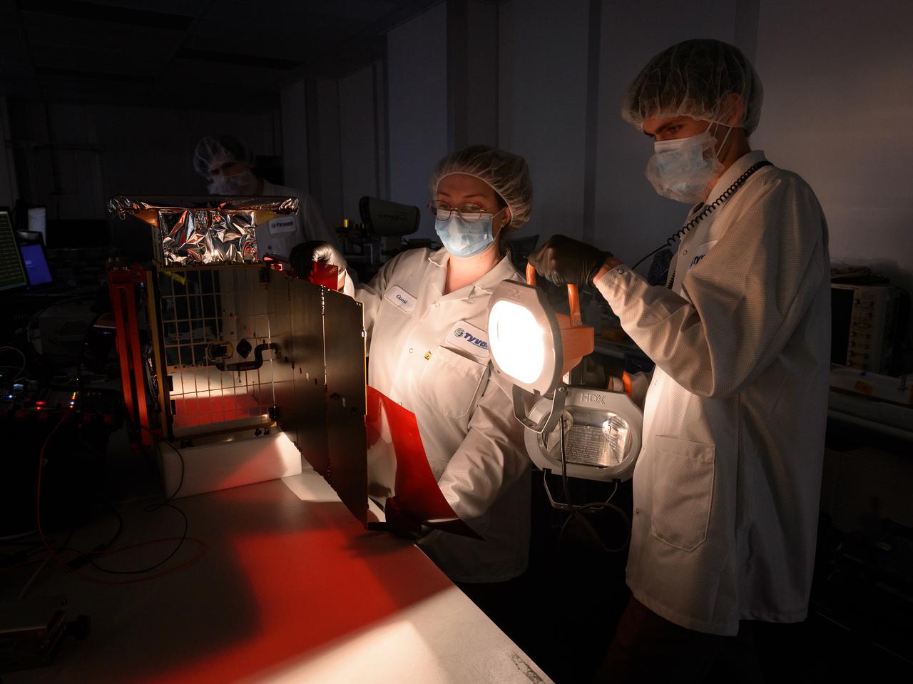 Rebecca Rogers, systems engineer, center, Lachlan Moore, systems integration engineer, right, and Dylan Schmidt, CAPSTONE assembly integration and test lead, background, perform a solar panel string voltage test of the CAPSTONE spacecraft at Tyvak Nano-Satellite Systems, Inc., in Irvine, California.