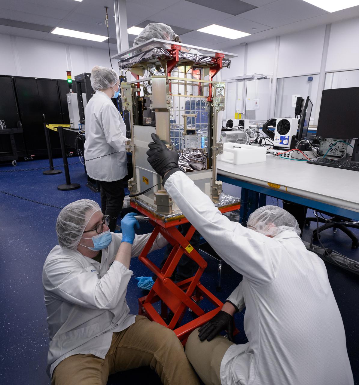 Matt Johnson, CAPSTONE lead systems engineer, bottom, Dustin Holta, launch engineer, right, and Rebecca Rogers, systems engineer, background, with the CAPSTONE spacecraft stowed in its dispenser at Tyvak Nano-Satellite Systems, Inc., in Irvine, California.