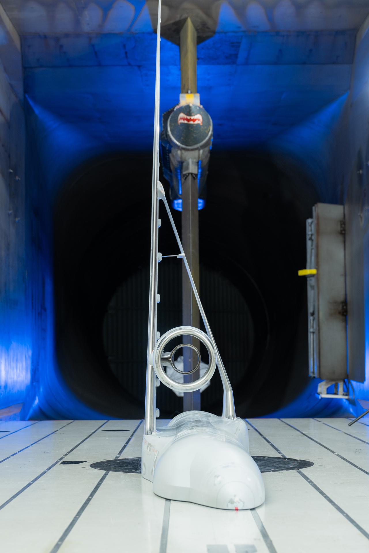 There is a half model of an airplane in the center of the photo that is painted white, the background of the photo is black in the center with blue lights all around the side. The floor that the half model of the plane sits on is white.