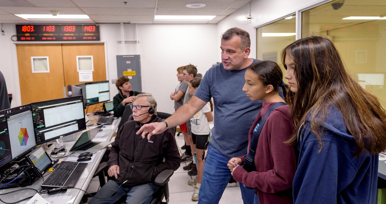 Chris Provencher explains the Volatiles Investigating Polar Exploration Rover (VIPER) mission to his family in the Multi-Mission Operations Center (MMOC), N240, for VIPER Family Day. Dennis Heher is seated at the control console at the left.