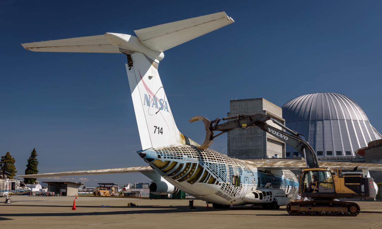 A Volvo Crawler Excavator severs the airframe, separating the tail section from the fuselage, of the modified C-141 Kuiper Airborne Observatory, (KAO) (NASA-714), on the N211 apron of Moffett Field, California.
