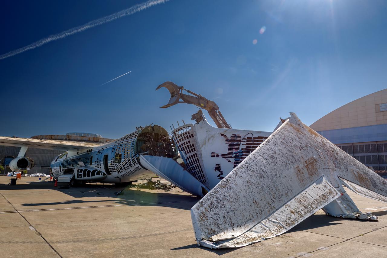 A Volvo Crawler Excavator severs the airframe, separating the tail section from the fuselage, of the modified C-141 Kuiper Airborne Observatory, (KAO) (NASA-714), on the N211 apron of Moffett Field, California.