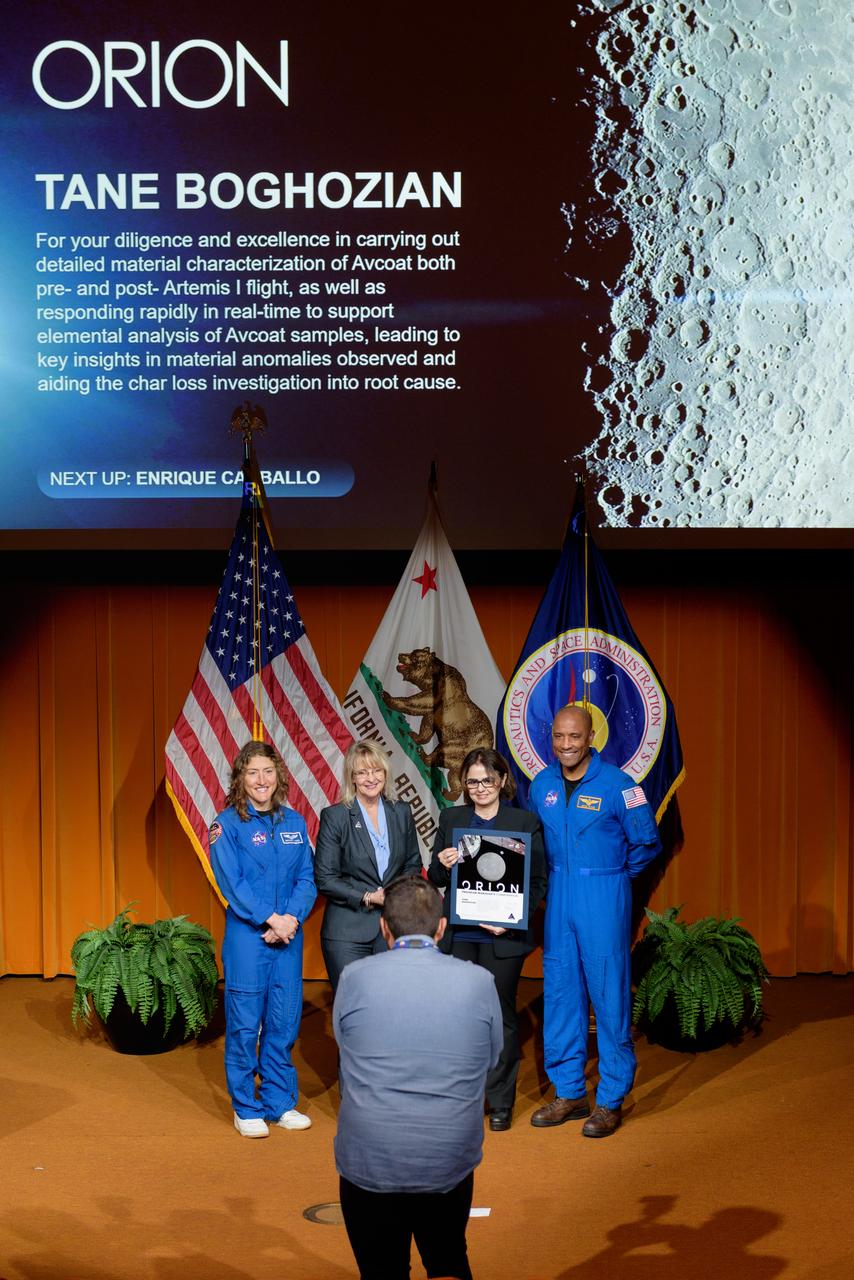NASA Ames staff photographer Brandon Torres Navarette, front, photographs Orion program manager’s commendation award presented to Tane Boghozian (ACD25-0023-005), center, by Orion Deputy Program Manager Debbie Korth, left, NASA astronauts Victor J. Glover, right, and Christina Koch, left, in the Syvertson Auditorium, N201.