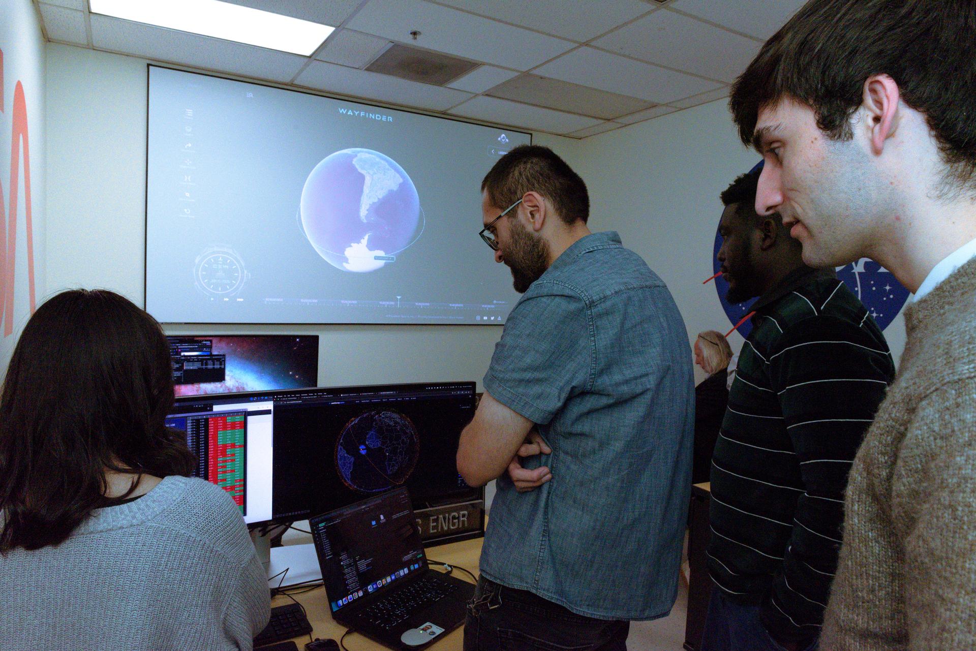 TechEdSat-11 operators Daphne Dao, left, Alejandro Salas, Kwabena Boateng, and Malachi Mooney-Rivkin, right, in the Ames Multi-Mission Operations Center (MMOC), N240 Annex, Eros control room 162. The team monitors the spacecraft's status during the Exo-Brake “parachute” deployment.   The ExoBrake is a drag device that increases the total surface area of the spacecraft to assist with a quicker deorbit. This maneuver is deployed at the end of mission to satisfy NASA's deorbit requirement and prevent space debris. TechEdSat has spent the last several months coordinating with NASA’s Conjunction Assessment Risk Analysis (CARA) team to ensure the spacecraft can safely deploy the ExoBrake without colliding into any other objects.