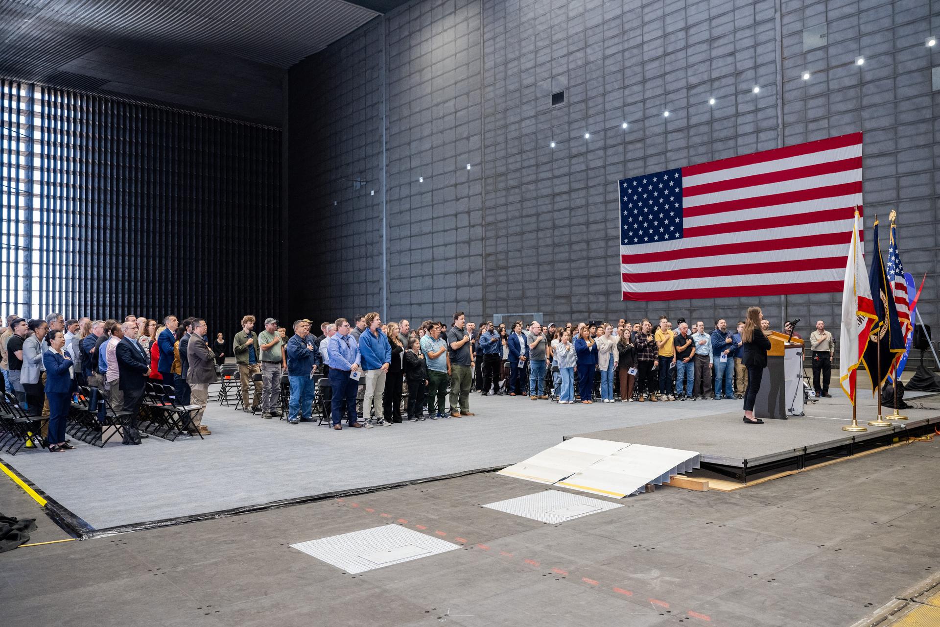 Attendees stand with MC Director of CAHR Linda Jensen for the National Anthem during the NASA Civil Servant Swearing-in Ceremony in the National Full-Scale Aerodynamics Complex (NFAC) 80-by-120-foot test section, N221.