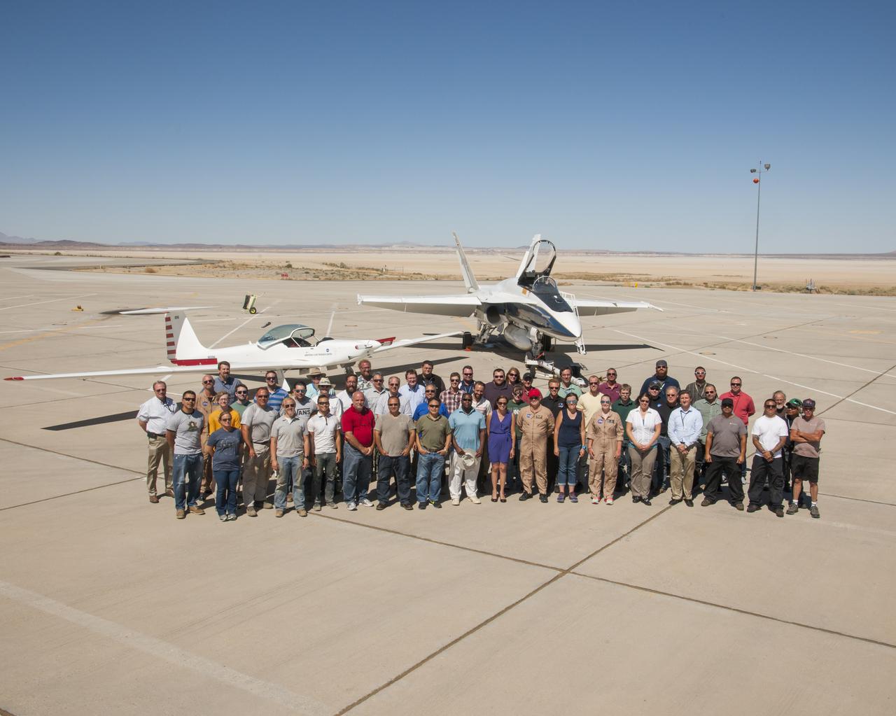 NASA’s SonicBAT team poses in front of the TG-14 motor glider and F/A-18 research aircraft, sitting side-by-side in front of Rogers Dry Lake prior to a SonicBAT flight at Armstrong Flight Research Center on Edwards Air Force Base, California. The TG-14 collected sound signatures of shockwaves created by the F/A-18, to compare with signatures collected on the ground.