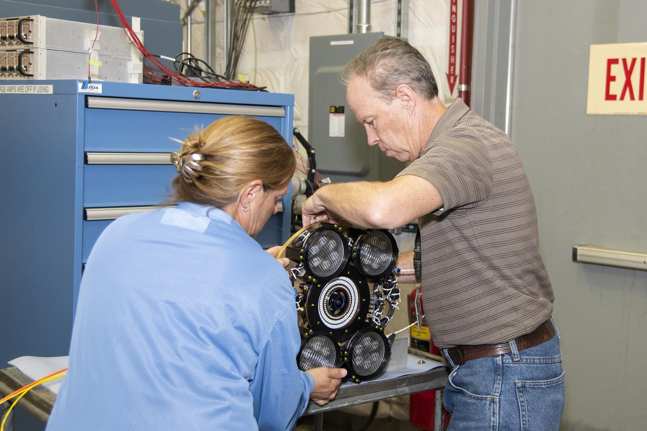 Dan Nolan, who with engineer Lucas Moxey developed the camera system shown in the photo, is seen working with April Torres to prepare it for vibration testing at NASA’s Armstrong Flight Research Center. The camera system is designed to operate as part of the Orion AA-2 test article’s abort test booster/separation ring developmental flight instrumentation subsystem. The testing proved the camera system could function and endure the predicted flight environment.