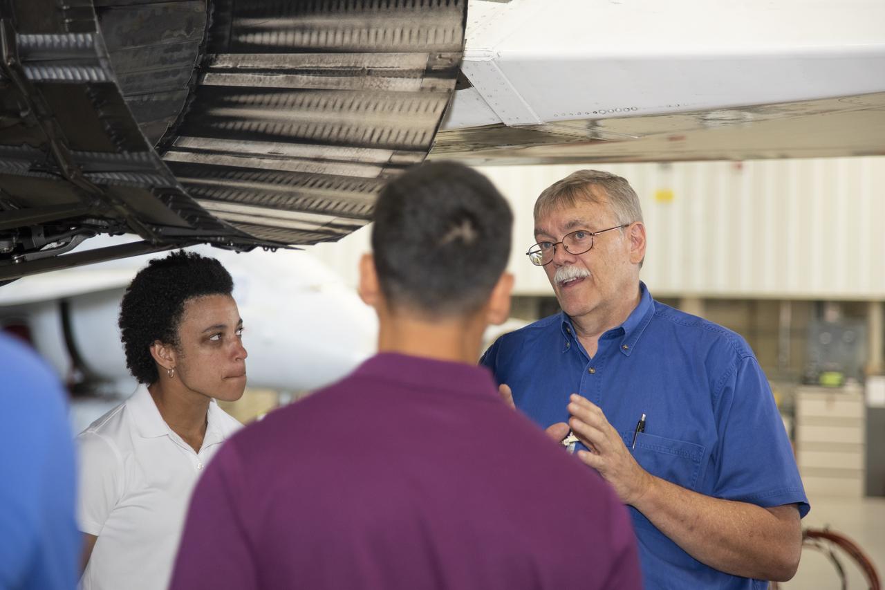 NASA's 2017 astronaut candidates toured aircraft hangar at Armstrong Flight Research Center, in Southern California where Crew Chief Tom Grindle talks with (L to R) Jessica Watkins and Raja Chari near engine nozzle of F-15 jet. The F-15 will fly in tandem with the X-59 QueSST during early flight test stages for the X-59 development.