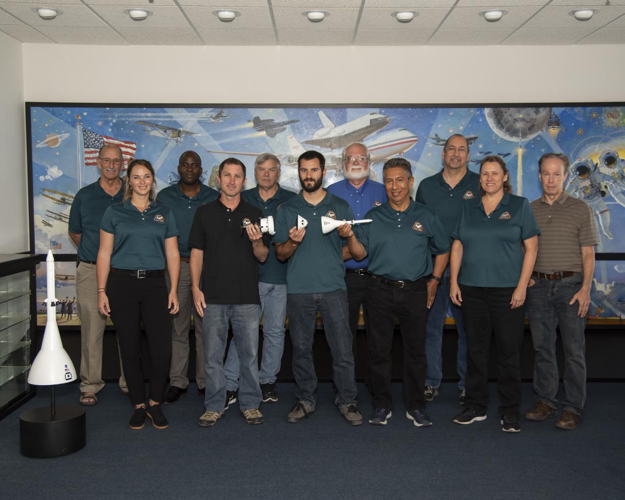 Members of the NASA Armstrong Flight Research Center Ascent Abort-2 management and engineering team contributed to the AA-2 launch at Cape Canaveral in Florida July 2, 2019. From left are Gary Martin, Rose Blomquist, Ernest Mwajagu, Lucas Moxey, Leo Gross, Jeff Sutherland, Chuck Rogers, Joe Hernandez, David Dowdell, Jeri Myers and Dan Nolan. Additional engineering team members include Paul Aristo, Bob Clark and Nikki Martin. Team members hold elements of the stack that was launched to show how the separation ring, crew module and Launch Abort System fit together.