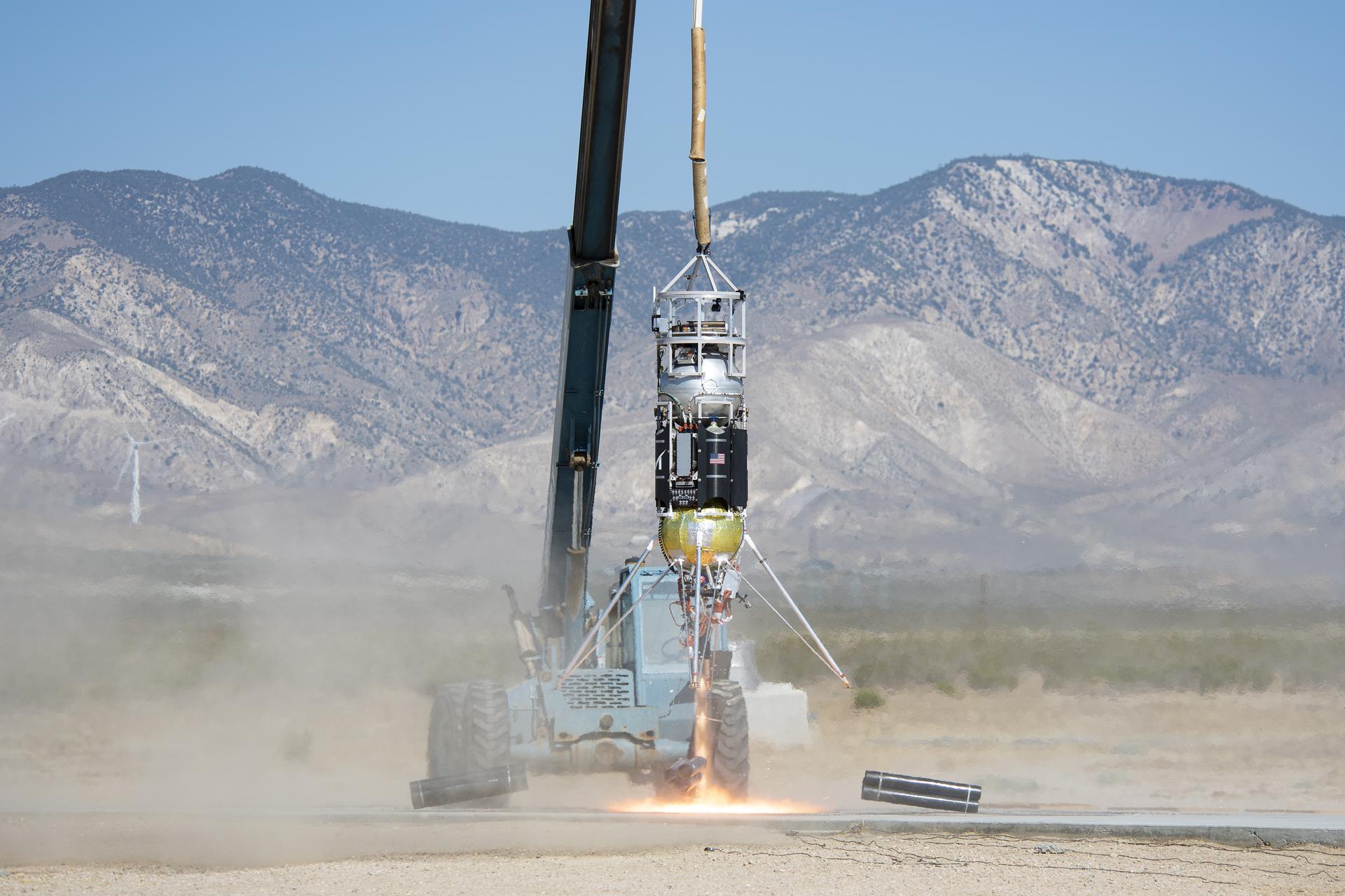 Xodiac lander lifts off tethered to a crane in the dessert.