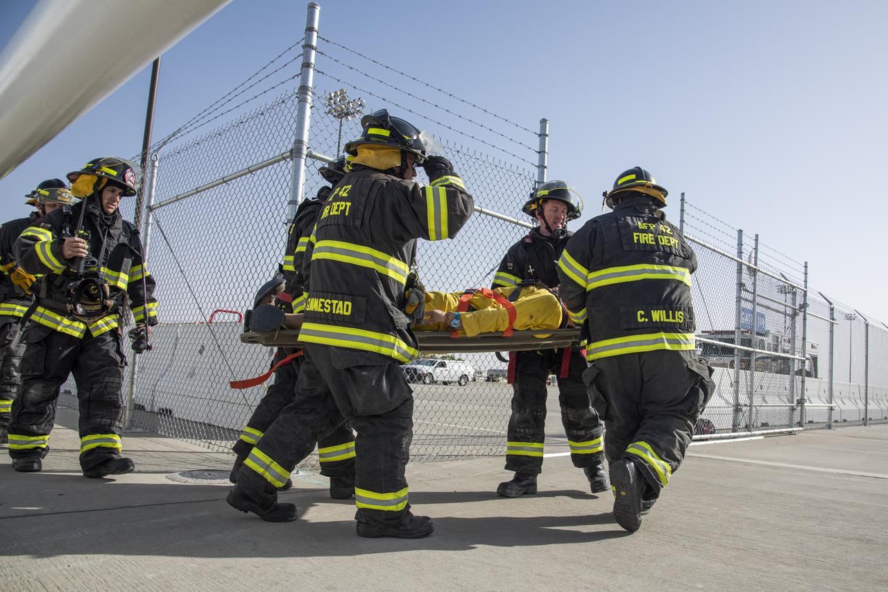 U.S. Air Force Plant 42 Fire Department responders carry out the mannequin to an emergency vehicle during an emergency exercise at NASA Armstrong Flight Research Center's Building 703 in Palmdale, California. Responders included, from left, Kent Courter, Doug Mendez, Alfonzo Ortega, Cedric Willis, Tyler Lippens and Ricky Gimmestad.