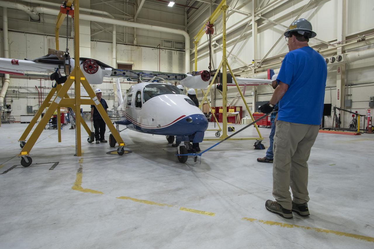 The X-57 fuselage is positioned under the Mod II wing section so that it can be reattached. The components were separated for transport to NASA's Armstrong Flight Research Center in California. Reintegration began shortly after the aircraft arrived. The X-57 is intended to help develop certification standards for emerging electric aircraft markets.