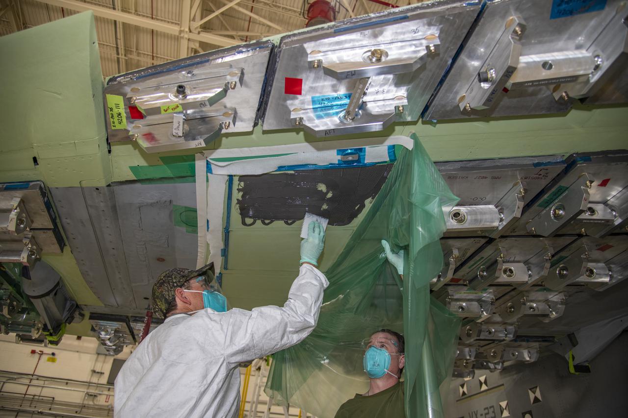 Ray Sadler, left, and Chris Mount spread tank sealant on the aircraft surface of a F/A-18E from the Naval Air Systems Command (NAVAIR) in Patuxent River, Maryland. The aircraft is in NASAâ€™s Armstrong Flight Research Center Flight Loads Laboratory in Edwards, California, for the centerâ€™s biggest load calibrations tests. This testing is needed before the aircraft can serve as a test vehicle for determining if it can safely manage maneuvers and proposed upgrades.