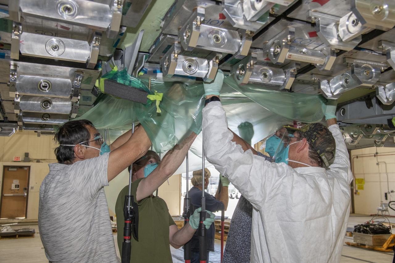 From left, Ronnie Haraguchi, Chris Mount, and Ray Sadler vacuum bag load pads on the aircraft surface of a F/A-18E from the Naval Air Systems Command (NAVAIR) in Patuxent River, Maryland. The aircraft is in NASA's Armstrong Flight Research Center Flight Loads Laboratory in Edwards, California, for the center's biggest load calibrations tests. This testing is needed before the aircraft can serve as a test vehicle for determining if it can safely manage maneuvers and proposed upgrades.