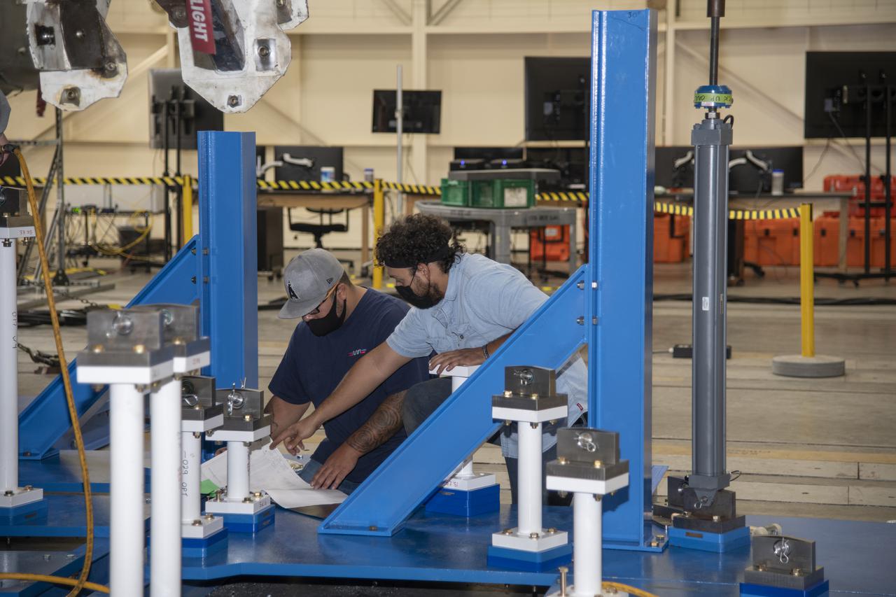 From left, Dominic Barela and Lucas Oramas review a drawing for installing the wing load test fixturing on a F/A-18E from the Naval Air Systems Command (NAVAIR) in Patuxent River, Maryland. The aircraft is in NASA’s Armstrong Flight Research Center Flight Loads Laboratory in Edwards, California, for the center’s biggest load calibrations tests. This testing is needed before the aircraft can serve as a test vehicle for determining if it can safely manage maneuvers and proposed upgrades. 