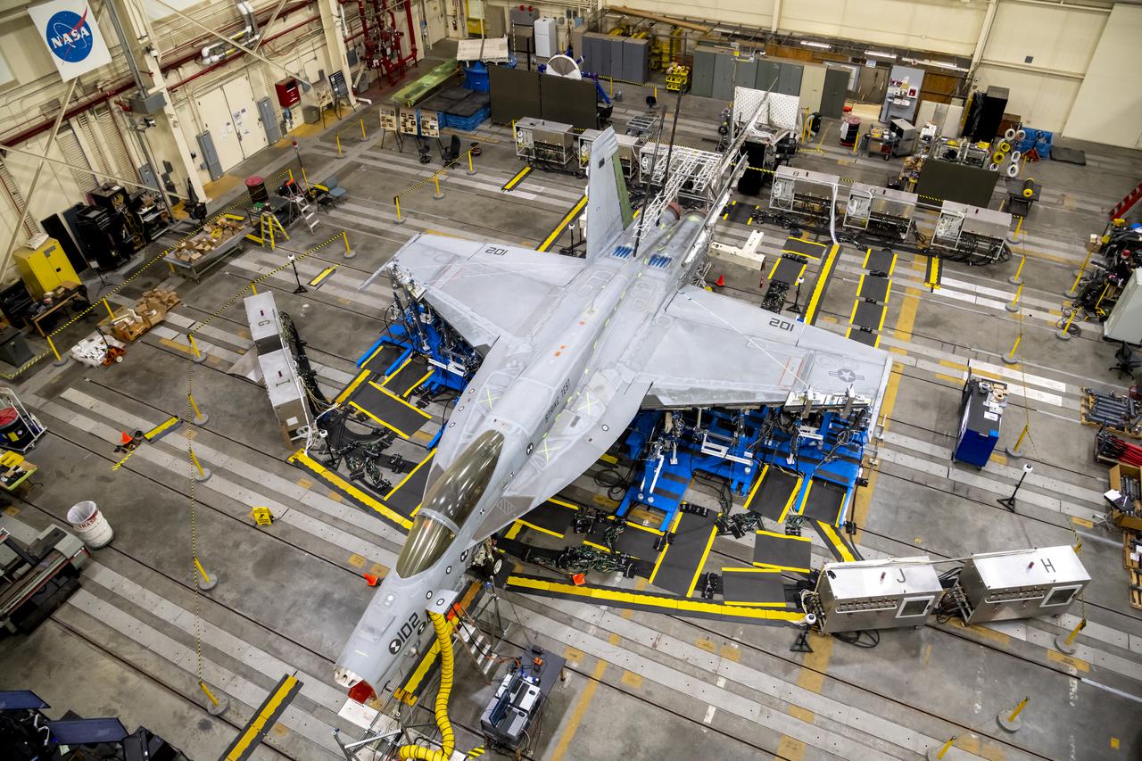 A top view shows the wing loading test configuration of a F/A-18E from the Naval Air Systems Command (NAVAIR) in Patuxent River, Maryland. The aircraft is in NASA’s Armstrong Flight Research Center Flight Loads Laboratory in Edwards, California, for the center’s biggest load calibrations tests. This testing is needed before the aircraft can serve as a test vehicle for determining if it can safely manage maneuvers and proposed upgrades. 