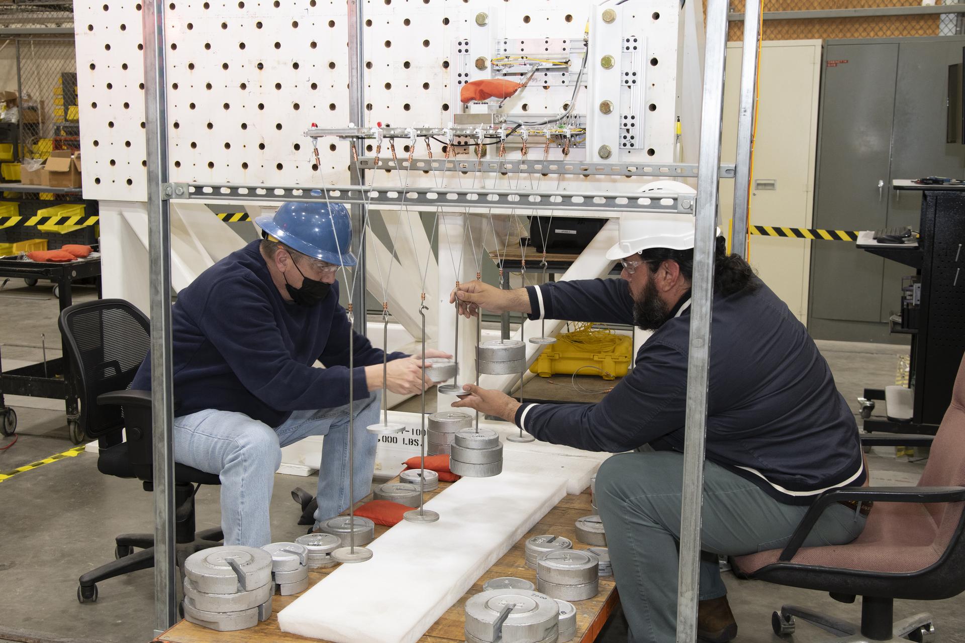 Two engineers carefully add weights to a model of a test aircraft wing.