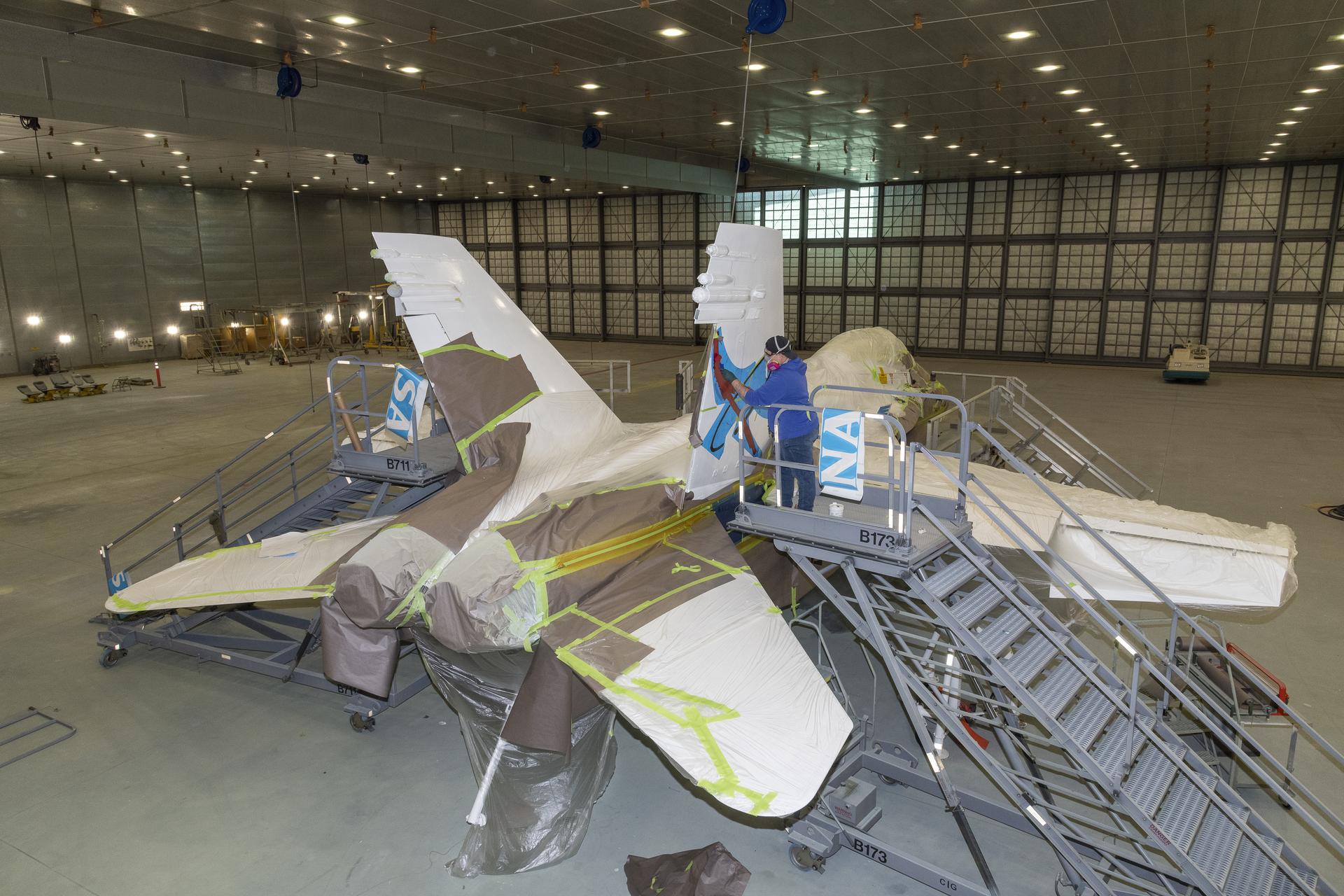 A person prepares to adhere NASA logos to the tails of a NASA aircraft.